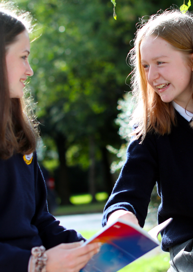 Two happy school girls reading a book and chatting